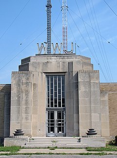 A white stone building with letters WWJ above it, and behind it, two broadcast towers are visible, one gray and one red and white