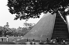 A tent-shaped building with a curved sloping triangular roof and layered with brown color