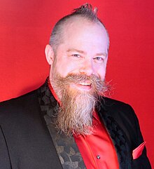 middle-aged Caucasian male in formal wear, with short hair and styled mustache and beard