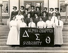 A group of 22 young Black women, posed for a photo with a banner