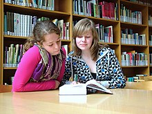 Two teenagers engage in joint attention by reading a book.