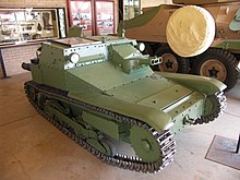 a green turret-less tracked vehicle inside a building