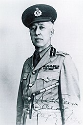 An older white man in a World War II era military uniform stands facing the camera.