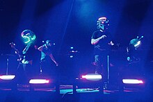 Coldplay onstage with their respective instruments and wearing custom helmets