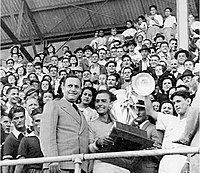 El presidente de la República de Costa Rica, Rafael Ángel Calderón Guardia, entrega el trofeo de campeón al arquero y capitán de la selección Hugo Zúñiga, (a su lado) y al entrenador Alejandro Morera Soto (de blanco).