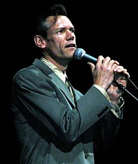 Singer Randy Travis, wearing a gray suit while singing into a microphone