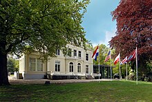 White building with law in front and flagpoles with flags flying