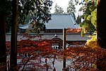 A building with large hip-and-gable roof beyond a roofed enclosure.