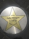 A circle-shaped plaque on the ground, with a gold-colored star on it. The texts "variety Kylie Minogue entertainer of the century" are written within the star.