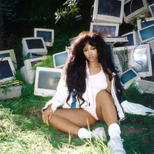 SZA sitting on the same patch of grass with the same backdrop of computer monitors, but with different angle and lighting