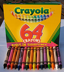 Crayola yellow and green sixty-four color box shown on a table with sixteen of the crayons from the box arrayed in front of it