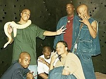 The group in 1996, on the set of the music video for Hit 'Em Up. Standing: Napoleon, E.D.I Mean and Hussein Fatal. Squatting: K.Kastro, Makaveli Tha Don and Yaki Kadafi.