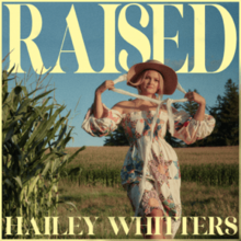 A photograph of Whitters walking through a field hearing a hat and a white patterned dress