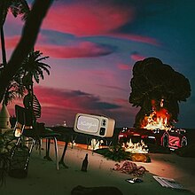 The album artwork for Nostalgia, which takes place on an island at sunset, with palm trees on the left. A broken-down car on fire appears behind a television, which reads "Nostalgia". A skeleton is also seen siting on a chair, with several items scattered around the ground; a bottle, bonfires, clothing, a phone and a newspaper.