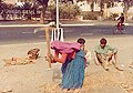 In New Delhi, a woman wields a pickaxe on a footpath maintenance project while her husband takes a break and her baby sleeps