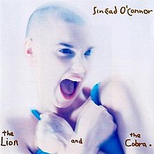 In a white background, Sinead O'Connor screaming while holding her arms in a crossed position.