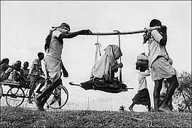 Two Muslim men (in a rural refugee train headed towards Pakistan) carrying an old woman in a makeshift doli or palanquin. 1947.