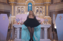 Sabrina Carpenter posing in front of pastel-colored coffins and other religious items inside a church.