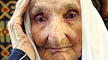 Photograph of an elderly, pale-skinned woman with a white headcovering.